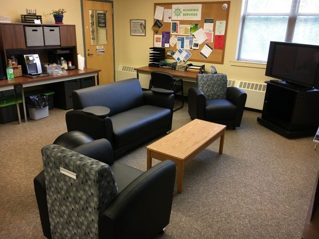 Shows couches surrounding a coffee table with desks in the background