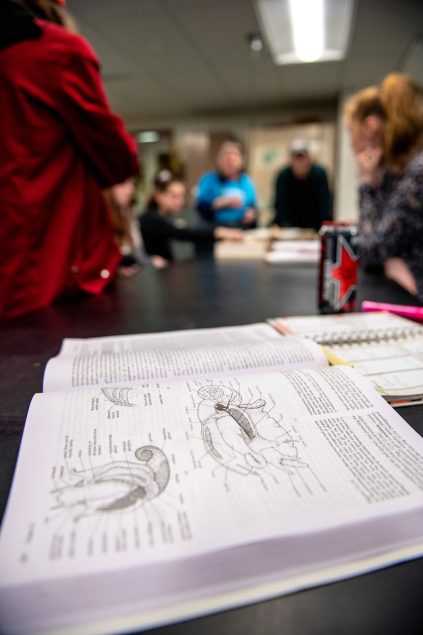 An open biology textbook in the foreground of a classroom