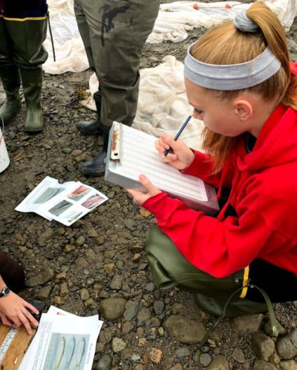 A student taking notes on a rocky beach