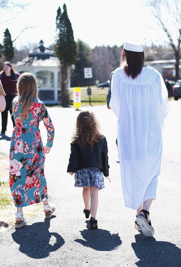 mother in cap and gown and two children walking away from the camera together