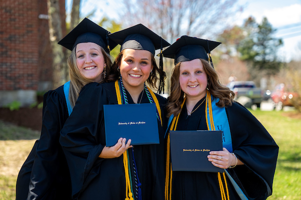3 graduates pose outside with their diplomas after graduation