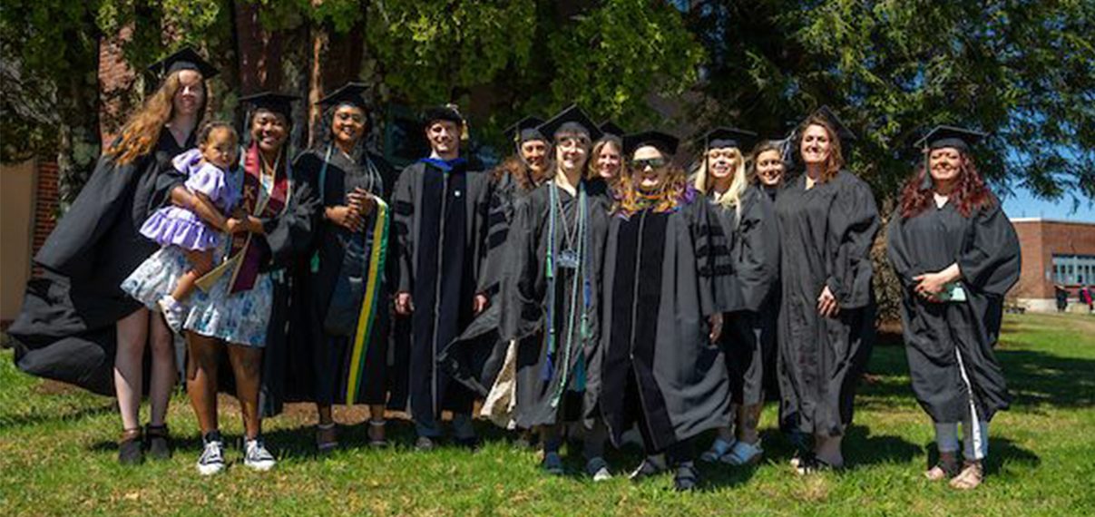 A group of students and faculty pose together outside before graduation.
