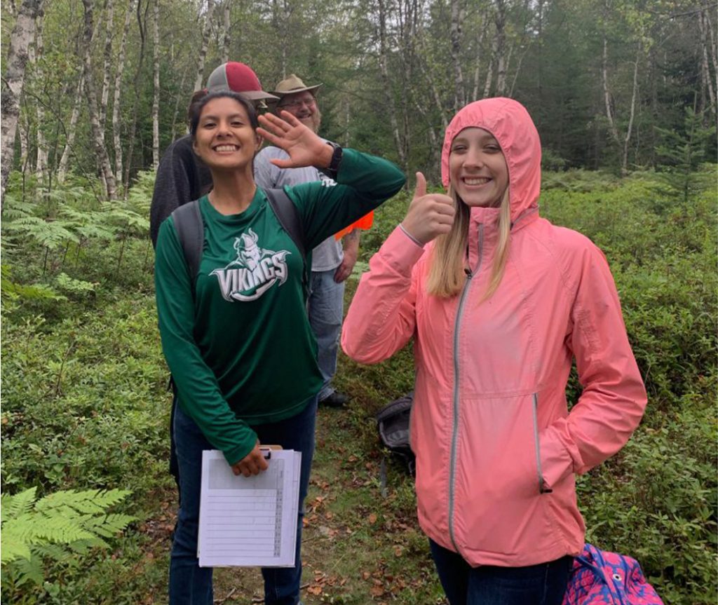 Students smiling and giving a thumbs up on a walk in the forest