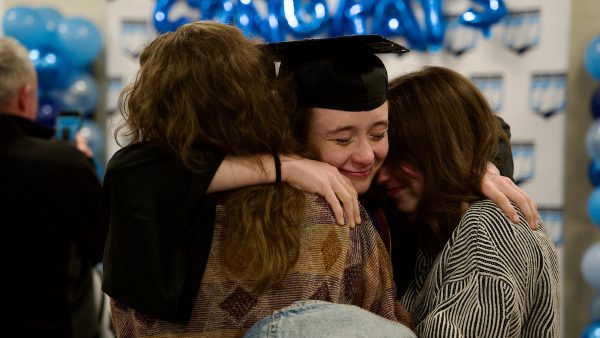 A graduate hugs two family members after graduation