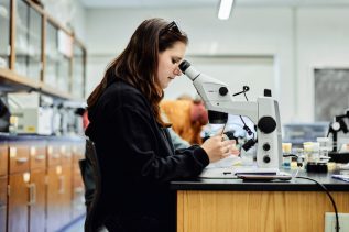 Student with long brown hair is looking into a microscope
