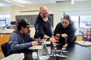 Dr Jones works with two students in a lab evaluating a sample