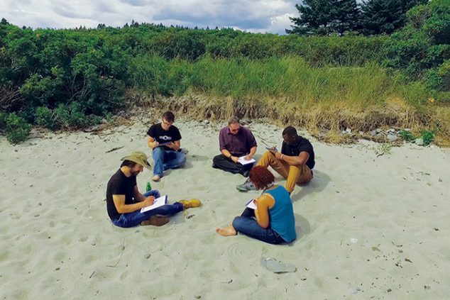 Four students and a professor sitting in the sand on a beach, in an outdoor writing workshop