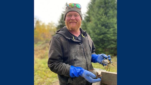 Sam is wearing waterproof overall and gloves and is holding 2 green crabs