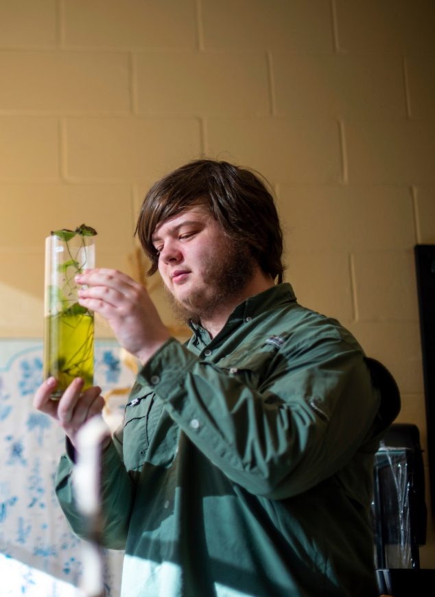 A student is holding a test tube with a piece of plant matter inside it