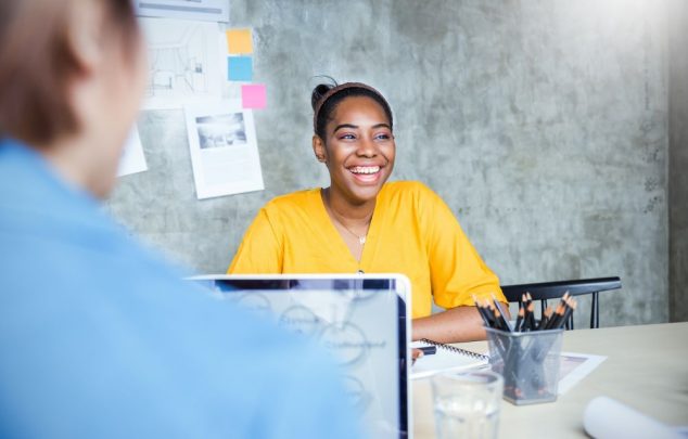 Young woman smiling with sticky notes on the wall behind her, in a business meeting