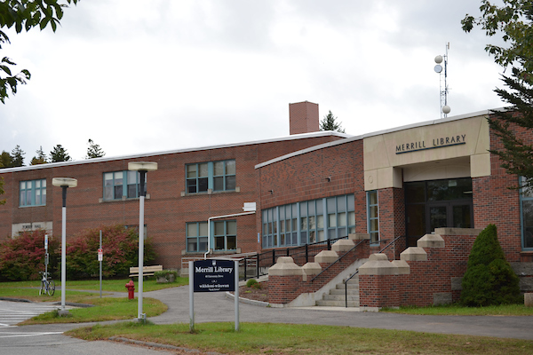 Outside of Merrill Library. A blue sign is in front of the building. Merrill Library is made of red brick.