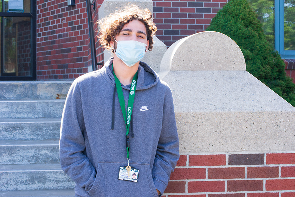 A young man in a hoodie is shown wearing a surgical mask in front of a brick entryway