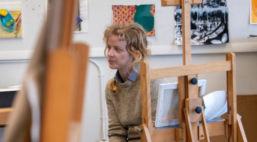 A student in a painting class is looking away from an easel