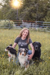 Morgan her her 3 puppies in a gated field, she's wearing a shirt that says "dog mom"