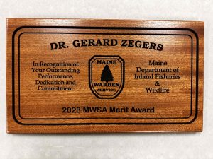 A wooden plaque that says Dr. Gerard Zegers "In recognition of your outstanding performance, dedication and commitment. It contains the Wardens Logo and the name of the award.