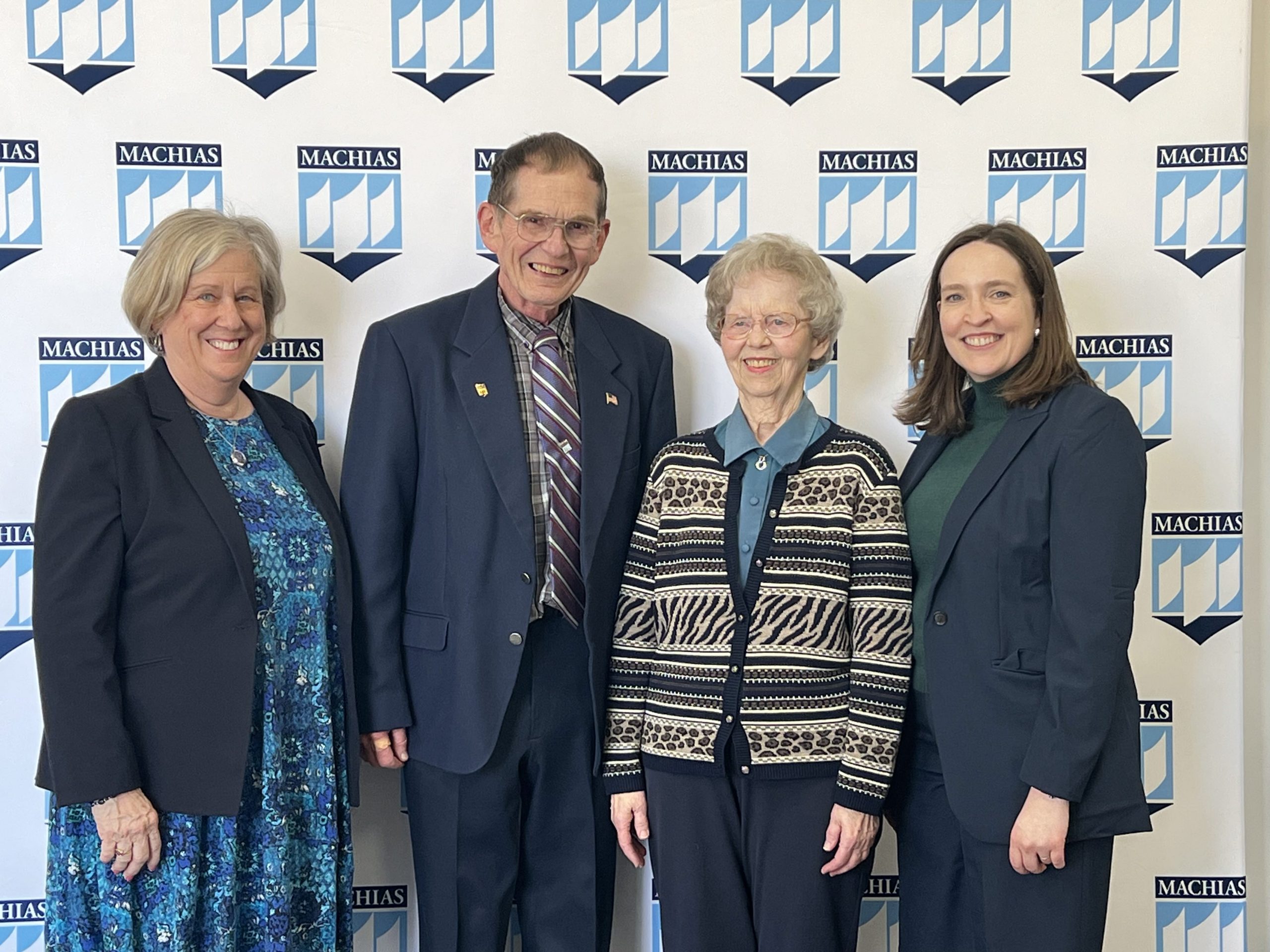 President Ferrini-Mundy, Richard Larson, Elsie Larson, Dean Megan Walsh, all pose in front of a UMaine Machis backdrop.