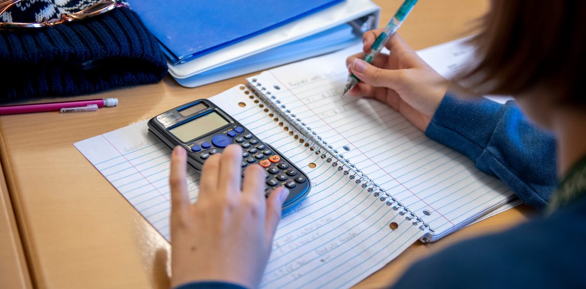 Hands of a student holding a pen and calculator over an open notebook