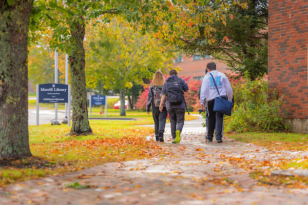 students walk away from the camera in front of the Science buildingon campus in the fall with leaves on the ground