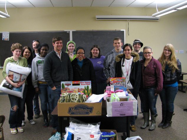 A group of students standing behind food drive collection boxes in a classroom