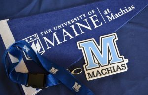 A blue pennant with the UMaine Machias logo in white, a blue lanyard with white "M" on it and a light blue "M" sticker with machias written below it.