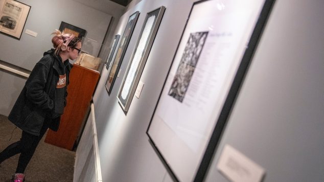 A student viewing a wall of framed artwork