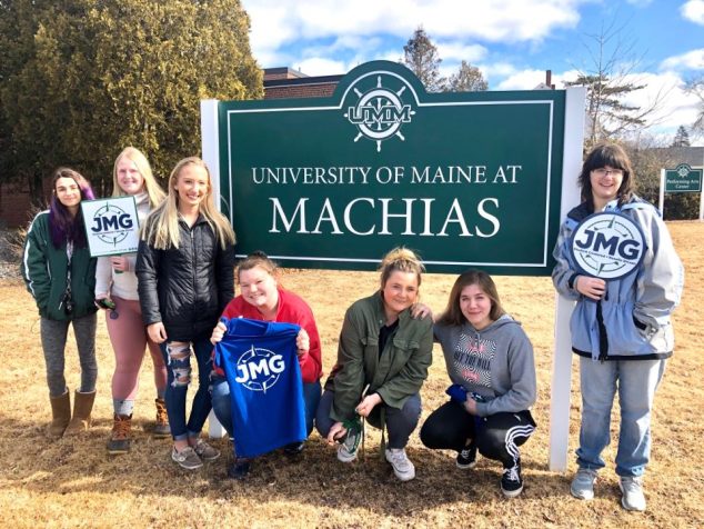 seven students with the University of Maine at Machias sign holding JMG signs and a t-shirt