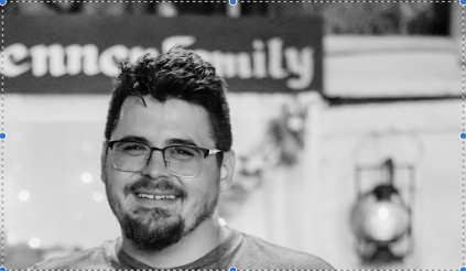 A black and white photo. Zach has short dark hair, a goatee and is wearing glasses.