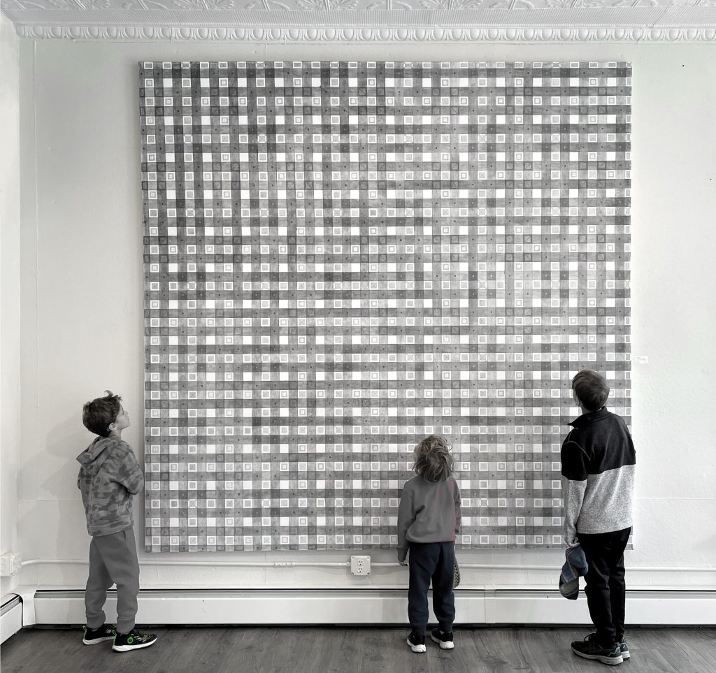 A black and whtie photo of a large checker pattern drawing with 3 people looking at it